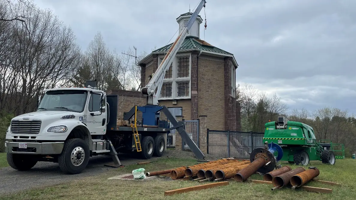 A truck set up to perform a well rehabilitation next to pipes sitting on the ground.